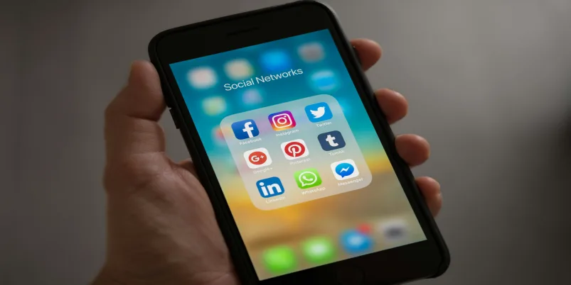 Persona sosteniendo teléfono inteligente con aplicaciones de redes sociales en la pantalla