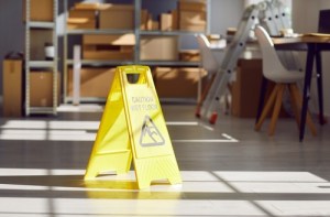 A caution sign on a wet supermarket floor with blurred shoppers in the background.