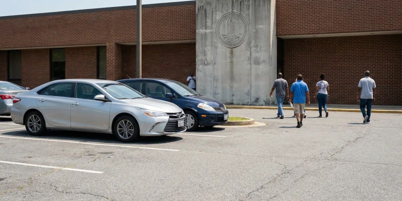 people walking toward brick government building entrance with official state seal